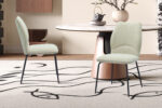 Twee ecru 'Lara' stoffen stoelen (2 per doos) staan bij een ronde tafel met een marmeren blad en licht houten onderstel, op een beige vloerkleed met zwarte abstracte motieven in een moderne eetkamer.