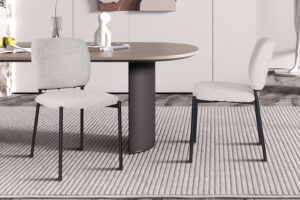 Twee PROMO - Stoel 'Sophia' Stof Beige stoelen (2 per doos) met metalen poten staan op een gestreept vloerkleed naast een ovale houten tafel in een moderne eethoek met minimalistische inrichting.