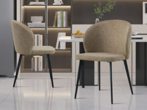 Twee Stoel 'Toledo' Stof Zand stoelen (2 per doos) met beklede beige stof en zwarte poten staan in een stijlvolle keuken, met planken met boeken en decor op de achtergrond, plus een wit aanrechtblad met een fruitschaal en vaas.