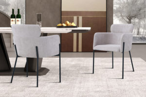 Een moderne eetkamer met twee Stoel 'Naomi' Stof Beige stoelen, een rechthoekige tafel met flessen, glazen en brood, een minimalistische inrichting en grote ramen die een winters tafereel buiten laten zien.