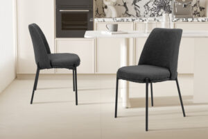 Twee moderne SALE - Stoel 'Ella' Stof Grijs stoelen (set van 2), met donkergrijze bekleding, staan in een minimalistische keuken met marmeren aanrechtblad, inbouwapparatuur en neutrale inrichting.