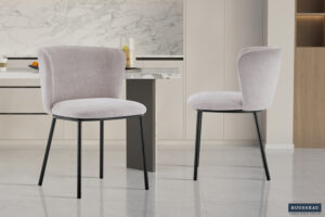 Twee Stoel 'Arthur' Stof Ote Belfast 23 Beige stoelen (set van 2) met beige bekleding en zwarte metalen poten staan in een moderne, minimalistische keuken met marmeren aanrechtblad en lichte kasten.