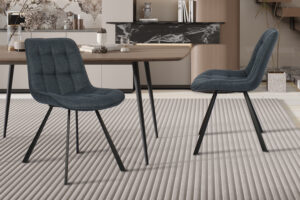 Twee Eetkamerstoel 'Ariba' stoelen in Ote Montego 303 donkerblauwe stof (set van 2) met zwart metalen poten staan op een licht vloerkleed met structuur in een moderne eetkamer met een houten tafel en minimalistische inrichting.