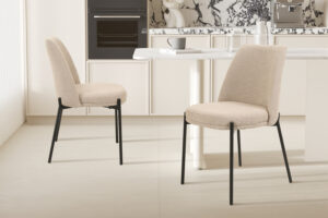 Twee 'Ella' stoelen in zandkleurige stof (SALE - Stoel 'Ella' Stof Zand, 2 per doos) met zwarte poten staan naast een witte keukentafel in een moderne keuken met marmeren achterwand en neutrale tinten.