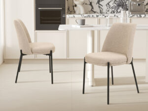 Twee 'Ella' stoelen in zandkleurige stof (SALE - Stoel 'Ella' Stof Zand, 2 per doos) met zwarte poten staan naast een witte keukentafel in een moderne keuken met marmeren achterwand en neutrale tinten.
