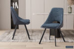 Two SALE - Eetkamerstoel 'Filou' Bouclé Blauw Vloerkleed PU Blauw stoelen (set van 2) met zwarte poten staan op een licht vloerkleed in een stijlvolle eetkamer met houten vloer, beige kasten, een marmeren tafel, boekenplank en decoratieve plant.