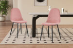 Twee Stoel 'Boy' Fluweel Roze stoelen met zwarte poten staan naast een rechthoekige tafel in een stijlvolle kamer met lichthouten vloeren, een vloerkleed met patroon, een plant en een minimalistische inrichting.