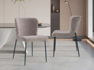 Twee Stoel 'Lisa' stoelen in stof Fabb Raven 30 Zand, met metalen poten, staan in een moderne eetkamer met een strakke tafel, decoratieve accenten en zachte neutrale tinten. (Verkocht per 2 per doos.).
