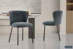 Twee moderne Stoel 'Arthur' Stof Ote Belfast 39 stoelen in donkergrijze stof (set van 2) met zwart metalen poten staan in een strakke keuken met marmeren achterwand, lichte kasten, gepolijste tegelvloer. Rousseau logo rechtsonder.