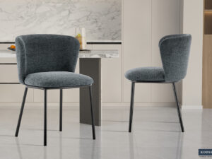 Twee moderne Stoel 'Arthur' Stof Ote Belfast 39 stoelen in donkergrijze stof (set van 2) met zwart metalen poten staan in een strakke keuken met marmeren achterwand, lichte kasten, gepolijste tegelvloer. Rousseau logo rechtsonder.