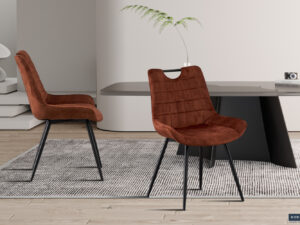 Twee Stoel 'Nina' Fluweel Roest stoelen met zwarte metalen poten staan op een grijs vloerkleed bij een strakke zwarte eettafel, geaccentueerd met minimalistische decoratie zoals een vaas met een plant en een kleine camera.