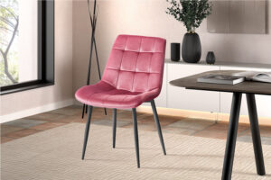 Een moderne kamer met Stoel 'Juta' Fluweel Roze stoelen (2 per doos) met zwarte poten, op een vloerkleed met een licht patroon. Een raam, een tegelvloer en een dressoir versierd met vazen en boeken maken de achtergrond compleet.
