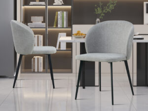 Twee Stoel 'Toledo' Stof Lichtgrijs stoelen (2 per doos) met zwarte metalen poten staan in een moderne keuken met glanzende vloeren, boekenplanken, een aanrecht met een schaal sinaasappels en een stijlvolle inrichting.