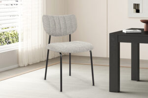 De Stoel 'Antura' Stof Ote Lisa 453 Lichtgrijs (2 per doos) heeft een moderne grijze bekleding en zwarte metalen poten, getoond op een licht vloerkleed in een minimalistische kamer bij een zwarte tafel en een raam met witte gordijnen.