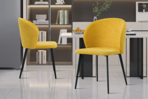 Twee gele stoffen 'Toledo'-stoelen (set van 2) met zwarte poten fleuren een keuken op met een wit aanrecht, een fruitschaal, planken met boeken en decor en een lichtgrijze tegelvloer.