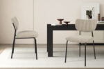 Twee 'Antura' Ote Lisa 170 stoffen stoelen (set van 2) staan bij een zwarte rechthoekige tafel in een minimalistische kamer met lichte muren, een vloerkleed en eenvoudige decoraties en kunstwerken op de achtergrond.