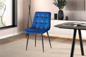 Een moderne eetkamer toont de Stoel 'Juta' Fluweel Blauw (2 per doos) met zwarte poten op een beige gedessineerd tapijt, naast een houten tafel en minimalistisch decor, tegen lichte muren en een groot raam.
