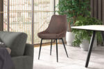 Een moderne woonkamer met twee Mirano bruine microfiber PU stoelen, zwarte metalen poten, grijze bank, marmeren tafel, grote planten in potten en ramen van vloer tot plafond met houten jaloezieën die natuurlijk licht binnenlaten.