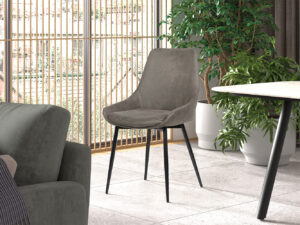 Een moderne woonkamer met de Stoel 'Mirano' Micro fiber PU Grijs stoel (2 per doos) op zwarte poten, geplaatst bij een grijze bank, ronde tafel, weelderige groene potplanten en hoge ramen met houten verticale lamellen voor natuurlijk licht.