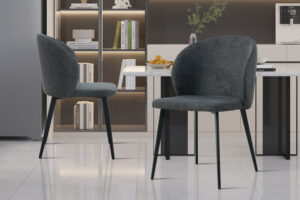 Twee Stoel 'Toledo' Stof Donkergrijs stoelen (set van 2) met zwarte metalen poten staan in een strakke keuken met een marmeren vloer, lichte kasten, een tafel met fruit en planken vol boeken en decor.