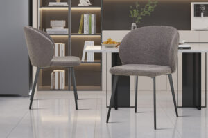 Twee SALE - Eetkamerstoel 'Toledo' Bouclé Grijs stoelen (set van 2) met metalen poten staan in een minimalistische keuken, aangevuld met een plank met boeken en decor, een tafel met fruit en zachte, gezellige verlichting.