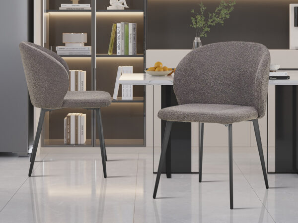Twee SALE - Eetkamerstoel 'Toledo' Bouclé Grijs stoelen (set van 2) met metalen poten staan in een minimalistische keuken, aangevuld met een plank met boeken en decor, een tafel met fruit en zachte, gezellige verlichting.