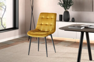 Een moderne eetkamer toont de Eetkamerstoel 'Juta' Fluweel Goud - geel fluwelen stoelen met zwarte metalen poten - op een licht gedessineerd tapijt naast een donkerhouten tafel en een minimalistische inrichting.