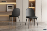Twee Stoel 'Jasmin' stoelen met PP zittingen en PU zwarte kussens (2 per doos) staan op een gepolijste marmeren vloer in een minimalistische kamer met beige kasten, houten planken, abstracte kunst en een decoratieve handsculptuur.
