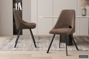 Twee Stoel 'Filou' Bouclé Zanddeken PU Bruin stoelen (set van 2) met zwarte poten staan op een lichtgrijs vloerkleed in een minimalistische eethoek met een marmeren tafel, neutraal getinte muren en achtergrondaccenten van boeken en een kleine plant.