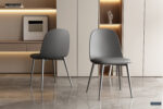 Twee Stoel 'Jasmin' stoelen in grijs met PP zittingen en PU kussens (set van 2) met metalen poten staan op een glanzende marmeren vloer in een minimalistische kamer met beige inbouwkasten, planken, boeken en een decoratieve handsculptuur.