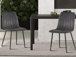 Twee moderne 'Willis' grijs fluwelen stoelen staan aan een donkere houten tafel op een licht vloerkleed, met een groene bladplant en decor op de achtergrond.
