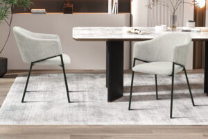 Twee 'Hugo' stoelen in lichtgrijs ribfluweel met zwarte metalen poten staan naast een rechthoekige eettafel met een licht marmeren blad op een grijs vloerkleed en creëren zo een eigentijdse, minimalistische setting.