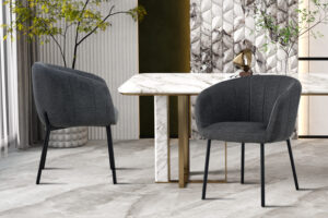 Twee Stoel 'Sevilla' Stof Donkergrijs stoelen (set van 2) met zwarte poten staan rond een rechthoekige marmeren tafel met gouden accenten, aangevuld met een decoratieve wand, kamerplanten en een lichte tegelvloer.