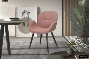 De SALE - Eetkamerstoel 'Maxim' Stof Roze (2 per doos), een roze gestoffeerde stoel met zwarte poten, staat op een grijs vloerkleed in een moderne kamer bij een tafel, abstracte kunst en planten met stenen bij de muur.