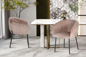 Twee moderne, gebogen Stoel 'Sevilla' Corduroy Fabb Hyper 38 Zand stoelen staan naast een wit marmeren eettafel met gouden accenten in een elegante kamer met gestructureerde muren, planten en decoratieve kunst.