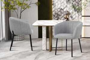 Twee Stoel 'Sevilla' Stof Lichtgrijs stoelen staan bij een wit marmeren tafel met gouden accenten in een stijlvolle kamer met gedessineerde muren, decoratieve planten en een neutrale vloer.