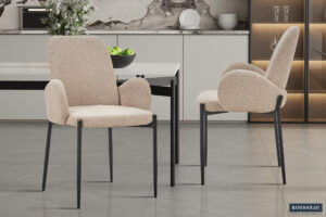 Twee Eetkamerstoel 'Bilbao' Bouclé Zand stoelen staan in een stijlvolle eetkeuken met een marmeren achterwand, witte tafel en een schaal met groene appels op het aanrecht.