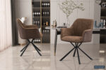 Twee 'Lucie' Bouclé Zand Vloerkleed PU Bruine stoelen (set van 2) met zwart metalen poten staan in een moderne eetkamer met een marmeren vloer, glazen tafel, planken met glazen en flessen, een vaas met takken en zonlicht door transparante gordijnen.