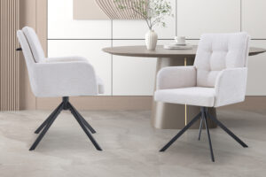 Twee Stoel 'Granada' stoelen in Davis Bliss 75-02 Ecru stof en zwarte metalen poten staan naast een ronde beige tafel met een witte vaas en beker. De scène heeft een lichte vloer en een minimalistische achtergrond. Set bevat twee stoelen per doos.