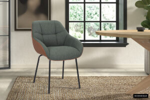 De SALE - Stoel 'Sem' heeft een groene stoffen bekleding en cognac PU zijkanten, hier getoond op een geweven vloerkleed in een lichte kamer met een groot raam, houten tafel en muurkunst. Verkocht als set van 2 per doos.