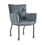 De Eetkamerstoel Thomas - Velvet Petrol is een moderne fauteuil met een petrolkleurige fluwelen zitting en rugleuning, zwarte metalen poten en vier wieltjes voor eenvoudige verplaatsing.