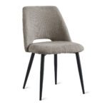 De Eetkamerstoel Monta - Taupe is een moderne eetkamerstoel met een zitting en rugleuning van beige structuurstof, een kleine uitsparing in de onderrug en vier slanke poten van zwart metaal.