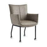 De Eetkamerstoel Thomas - Microleder Taupe is een moderne fauteuil met taupekleurige microleder bekleding, een gewatteerde zitting en rugleuning, zwarte metalen poten op vier wieltjes, met een strak, minimalistisch design en afgebeeld tegen een witte achtergrond.