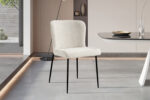 In een moderne eetkamer staan de Stoel 'Lisa' Bouclé Ecru stoelen met slanke zwarte metalen poten naast een strakke eettafel versierd met decoratieve schalen en glaswerk. De ruimte heeft lichtgrijze vloeren en een minimale inrichting.