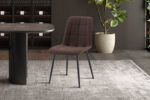 Een set van 4 moderne 'Furas' stoelen in donkerbruin PU staat op een gestreept tapijt naast een ronde zwarte tafel in een moderne kamer met een grote potplant en wandpanelen met structuur.