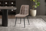 Een set van vier 'Furas' vintage bruine PU-stoelen staat op een licht vloerkleed naast een zwarte ovale tafel in een stijlvolle kamer met donkere planken en een potplant op de achtergrond.