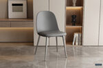 De Stoel 'Jasmin' Zitting PP kussen PU Grijs stoelen (2 per doos) met metalen poten geven een modern tintje aan een minimalistische kamer met een marmeren vloer, ingebouwde planken met boeken, decor en lichthouten kasten op de achtergrond.