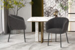 Twee SALE - Eetkamerstoel 'Sevilla' Bouclé Grijs stoelen staan naast een rechthoekige witte marmeren tafel met gouden accenten in een stijlvolle, eigentijdse kamer met gedessineerde muren en decoratieve planten.