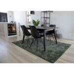 Een moderne eethoek met een Oslo Dining Chair set in zwart rond een zwarte tafel op een groen vloerkleed, geplaatst in een lichte kamer met lichte houten vloeren en een aangrenzende keuken zichtbaar op de achtergrond.