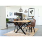 Een moderne eethoek heeft een ronde houten tafel en vier Stockholm Dining Chairs in lichtbruin vintage met zwarte poten. Hanglampen hangen erboven, decoratieve voorwerpen staan op tafel en de woonkamer met planten, bank en muurkunst is erachter zichtbaar.